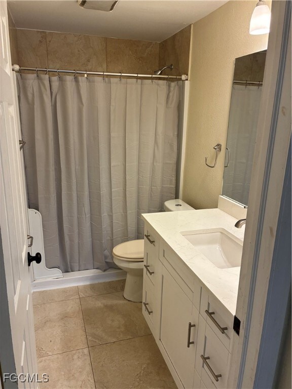 Full bathroom with a textured wall, vanity, and light tile patterned floors