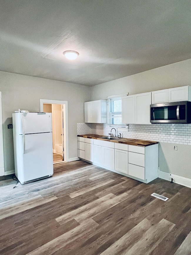 Kitchen with white cabinetry, freestanding refrigerator, dark wood-style floors, decorative backsplash, and stainless steel microwave