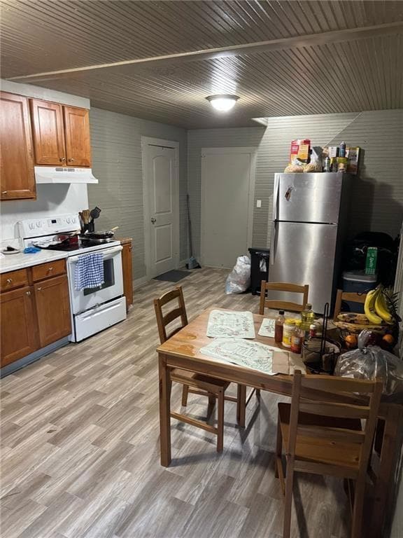 Kitchen with brown cabinetry, white electric stove, light countertops, light wood-style flooring, and freestanding refrigerator