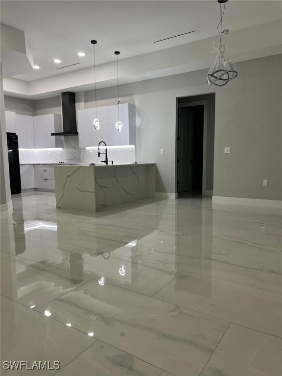 Kitchen with modern cabinets, white cabinetry, wall chimney exhaust hood, light marble finish floors, and pendant lighting