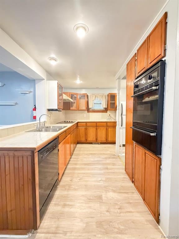Kitchen with brown cabinetry, glass insert cabinets, light wood finished floors, tile counters, and a warming drawer