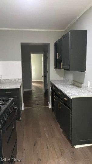 Kitchen with crown molding, black gas range oven, dark cabinets, dark wood finished floors, and light stone countertops