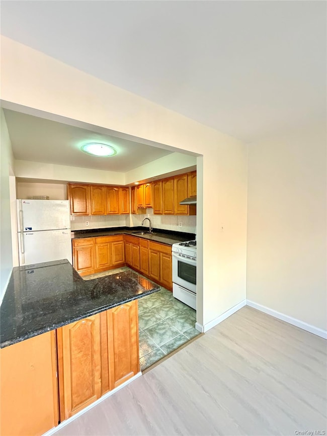 Kitchen featuring brown cabinets, white appliances, light wood-style floors, dark stone countertops, and a peninsula