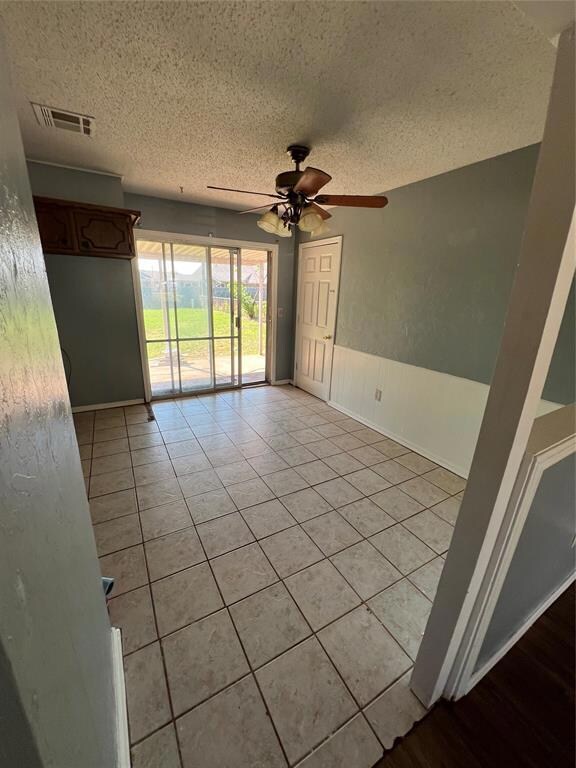 Tiled empty room with a textured ceiling and ceiling fan