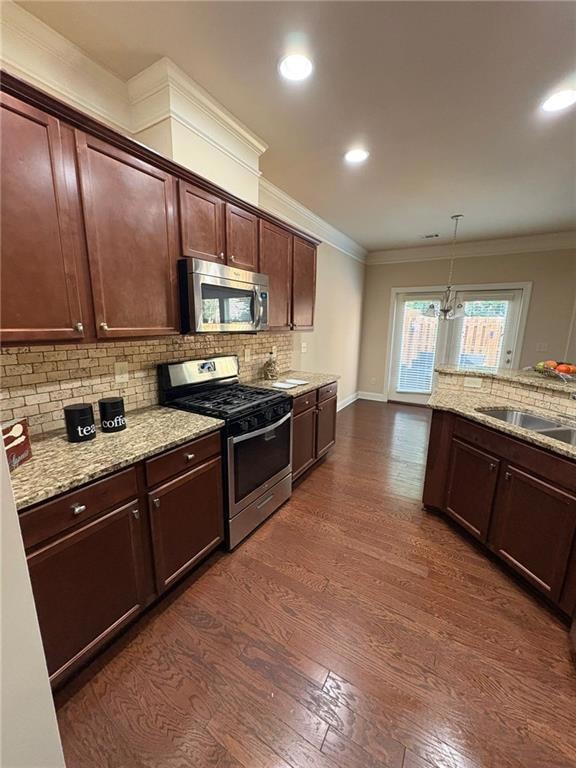 Kitchen with appliances with stainless steel finishes, backsplash, dark wood finished floors, light stone counters, and crown molding