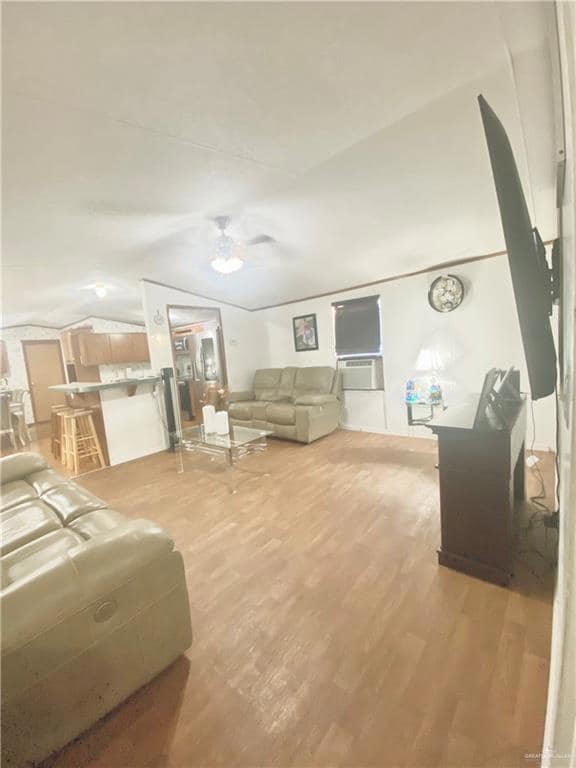Living room featuring light wood-style flooring, ceiling fan, vaulted ceiling, and cooling unit