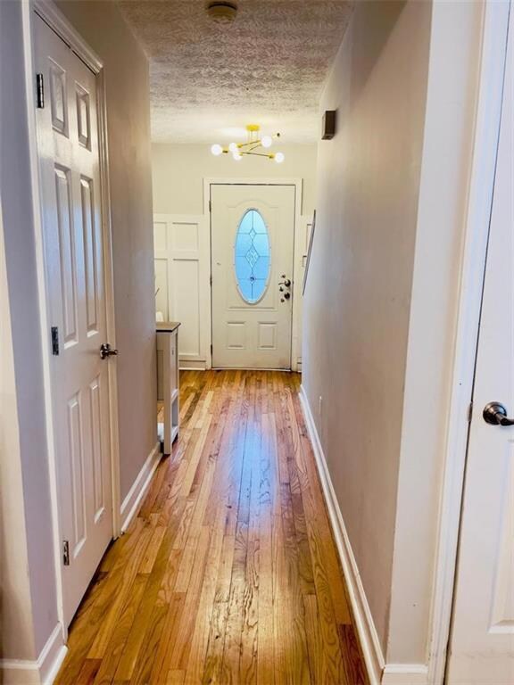 Doorway featuring light wood-style floors, baseboards, and a textured ceiling