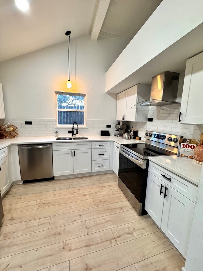 Kitchen with appliances with stainless steel finishes, white cabinetry, and wall chimney exhaust hood