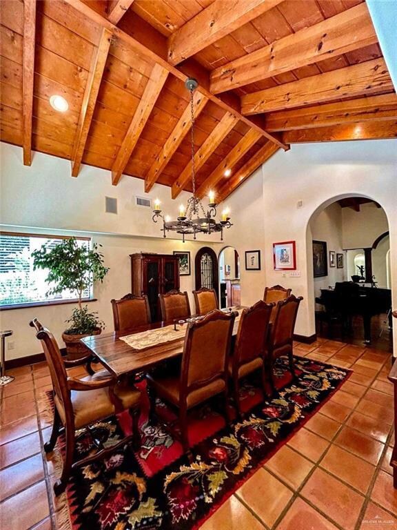 Dining area with an inviting chandelier, beamed ceiling, light tile floors, high vaulted ceiling, and wooden ceiling