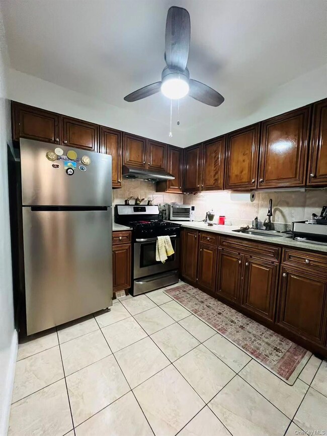 Kitchen featuring dark brown cabinetry, stainless steel appliances, tasteful backsplash, light tile patterned floors, and light countertops