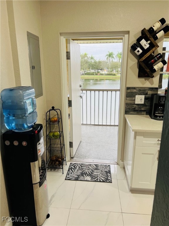 Kitchen with white cabinetry, electric panel, light tile patterned floors, a water view, and a textured wall