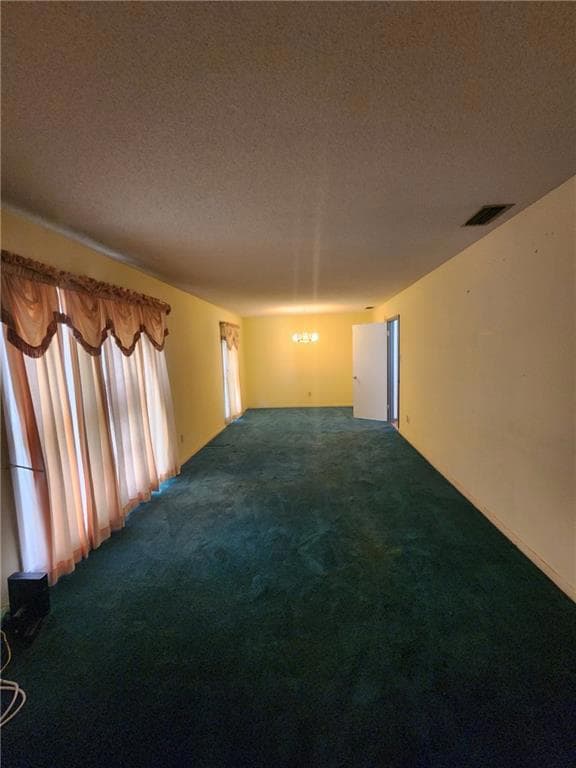 Empty room with dark colored carpet and a textured ceiling