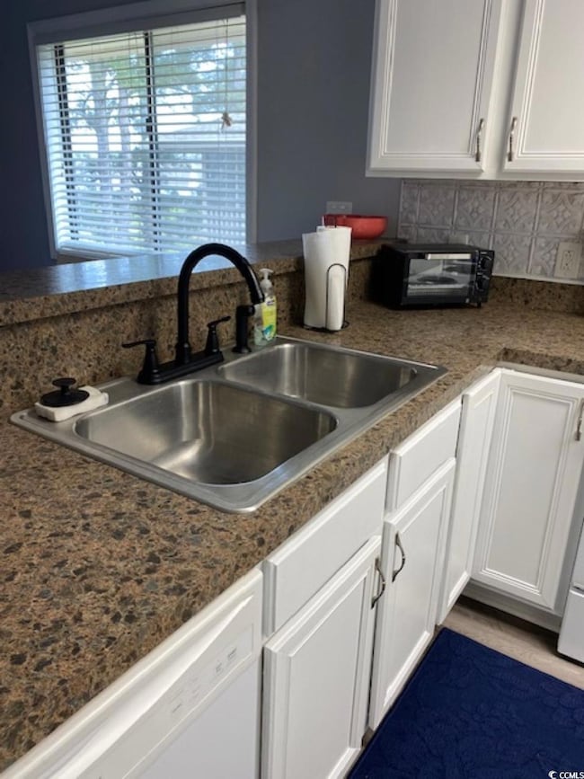 Kitchen featuring white dishwasher, a sink, white cabinetry, and backsplash