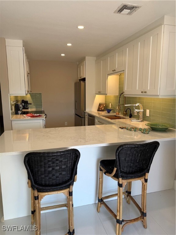 Kitchen with refrigerator, sink, a breakfast bar area, white cabinets, and kitchen peninsula
