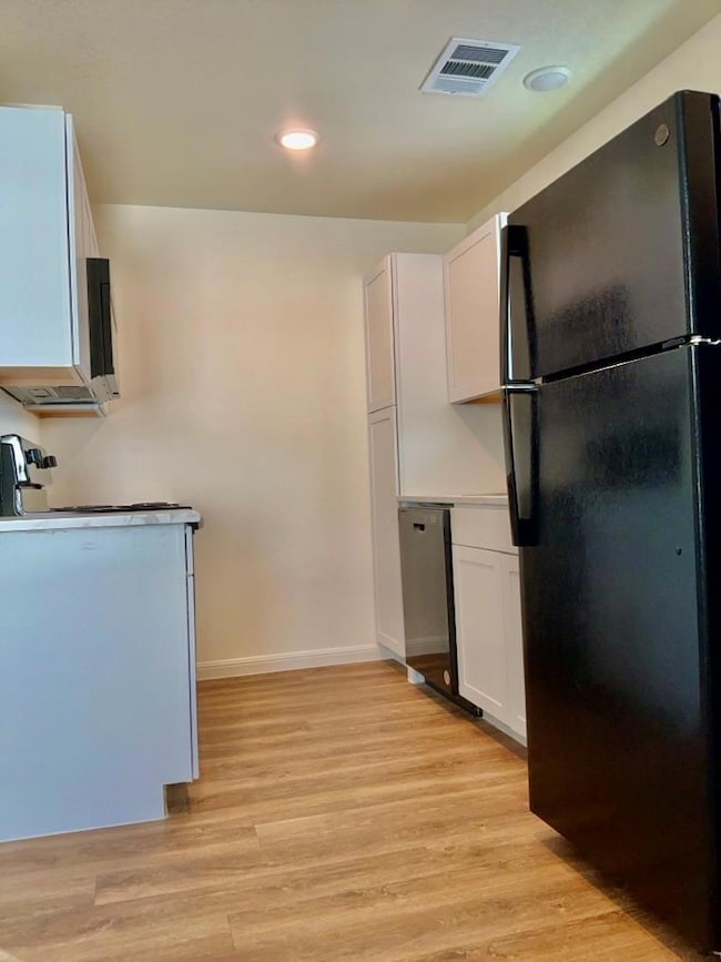 Kitchen with white cabinetry, black appliances, recessed lighting, light wood-type flooring, and light countertops