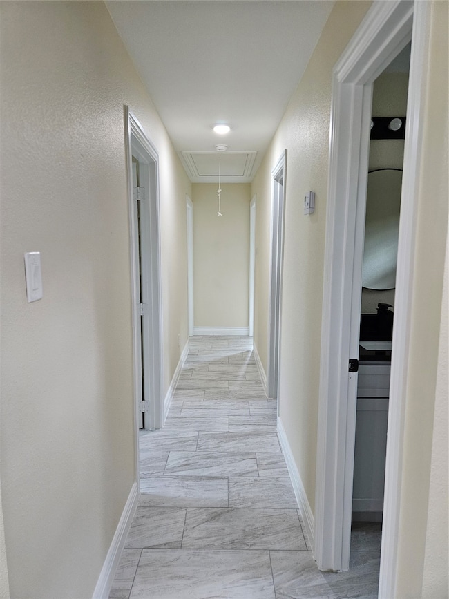 Hallway with attic access and baseboards