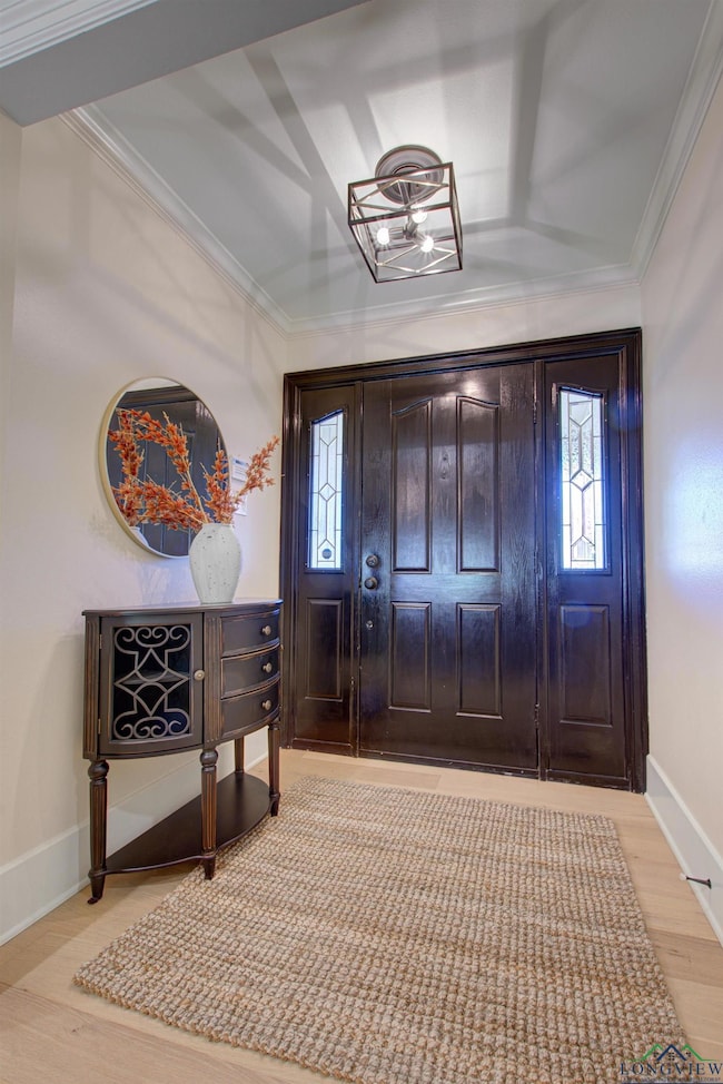 Foyer entrance with crown molding, baseboards, and light wood-style floors