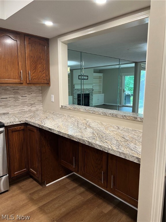 Kitchen with tasteful backsplash, hardwood / wood-style floors, a stone fireplace, dark brown cabinetry, and light stone countertops