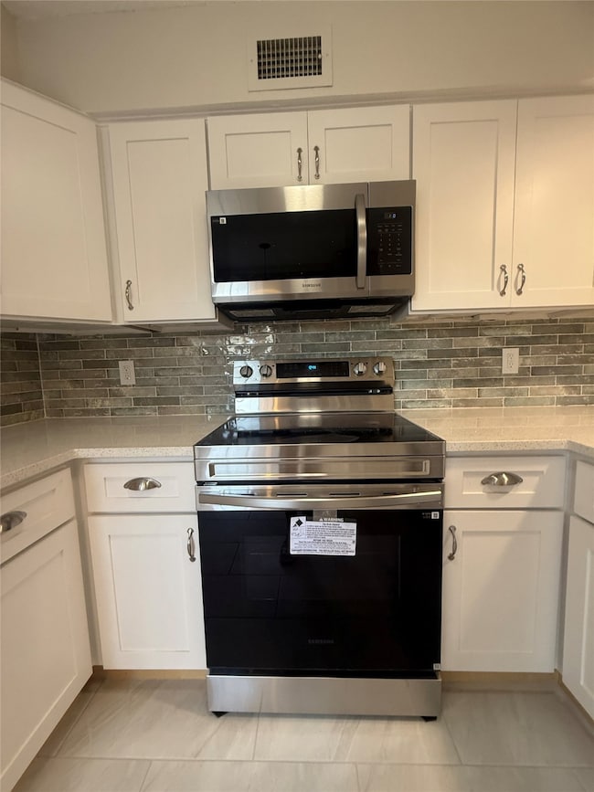 Kitchen with stainless steel appliances, white cabinetry, tasteful backsplash, and light stone counters