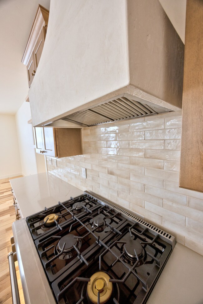 Kitchen with tasteful backsplash, premium range hood, gas stove, and light hardwood / wood-style flooring