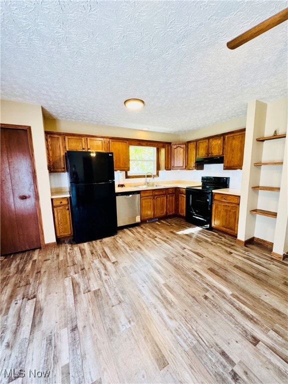 Kitchen featuring brown cabinetry, black appliances, light wood-type flooring, light countertops, and a textured ceiling
