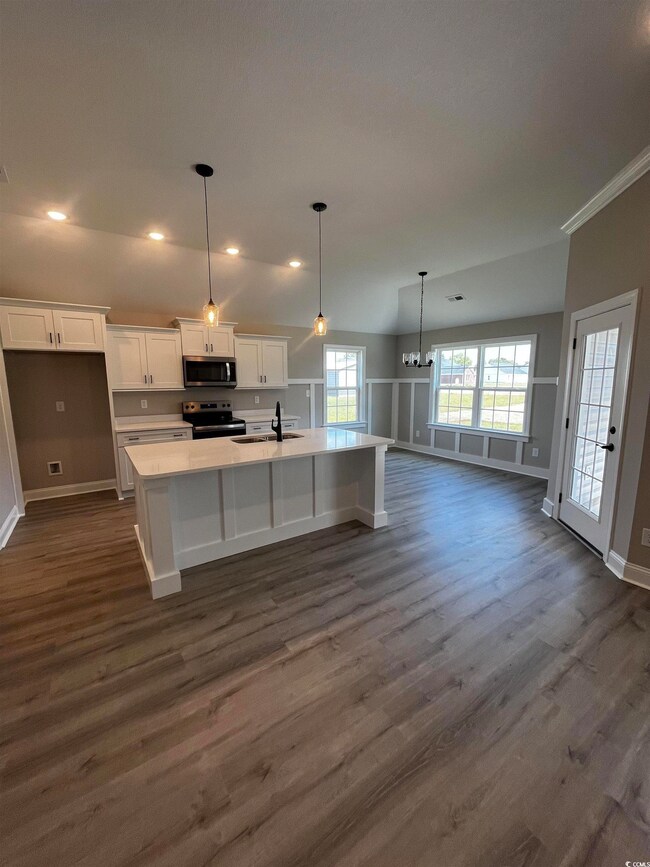 Kitchen with a kitchen island with sink, white cabinetry, pendant lighting, appliances with stainless steel finishes, and a kitchen breakfast bar