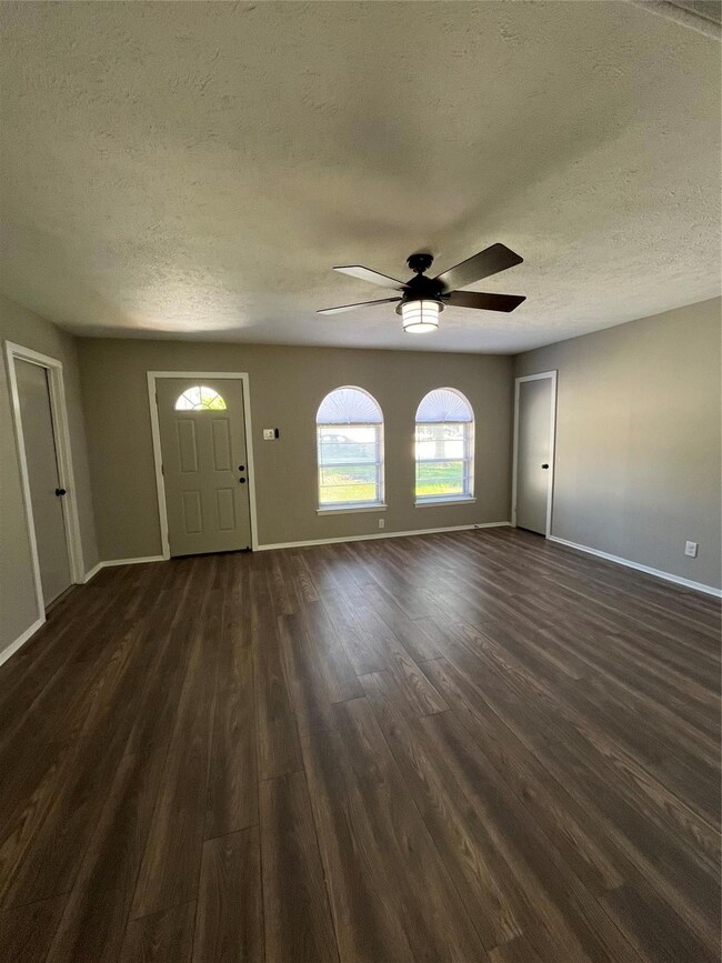 Empty room featuring a textured ceiling, ceiling fan, and dark wood-type flooring