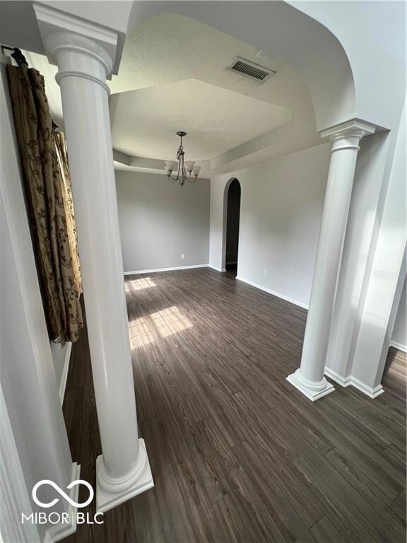 unfurnished living room featuring visible vents, a tray ceiling, arched walkways, ornate columns, and dark wood-style flooring