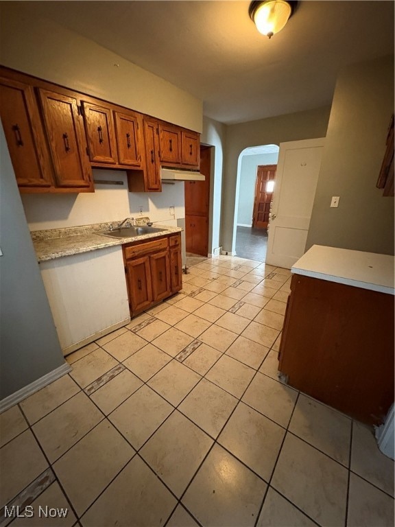 Kitchen with brown cabinets, light countertops, arched walkways, light tile patterned floors, and range hood