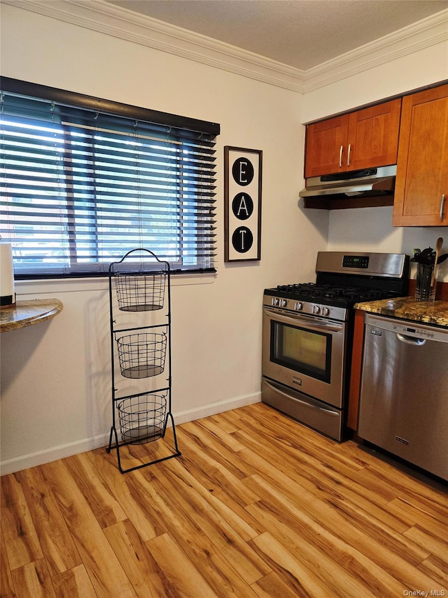 Kitchen with ornamental molding, stainless steel appliances, light wood-style floors, under cabinet range hood, and brown cabinetry
