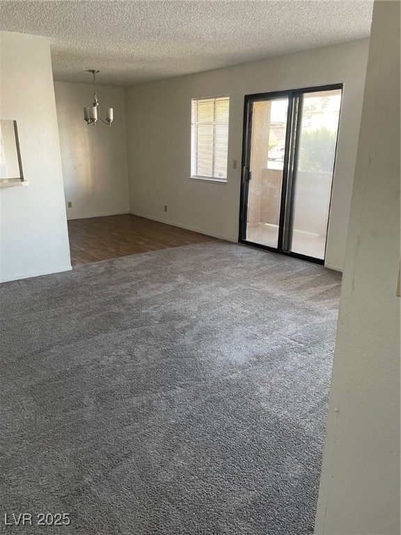 Spare room with dark carpet, a chandelier, and a textured ceiling