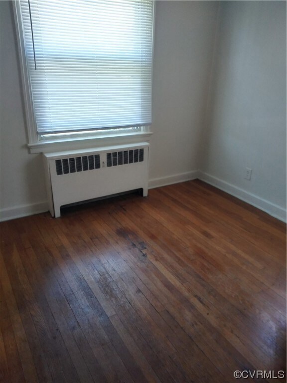 Unfurnished room featuring dark hardwood / wood-style flooring and radiator heating unit