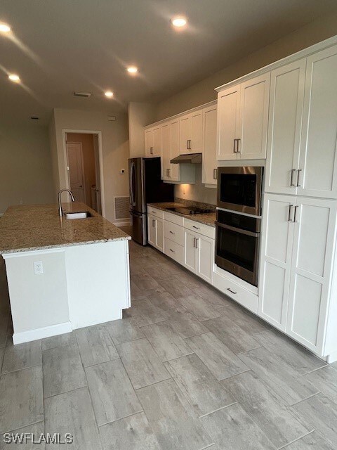 Kitchen with a sink, white cabinetry, stovetop, an