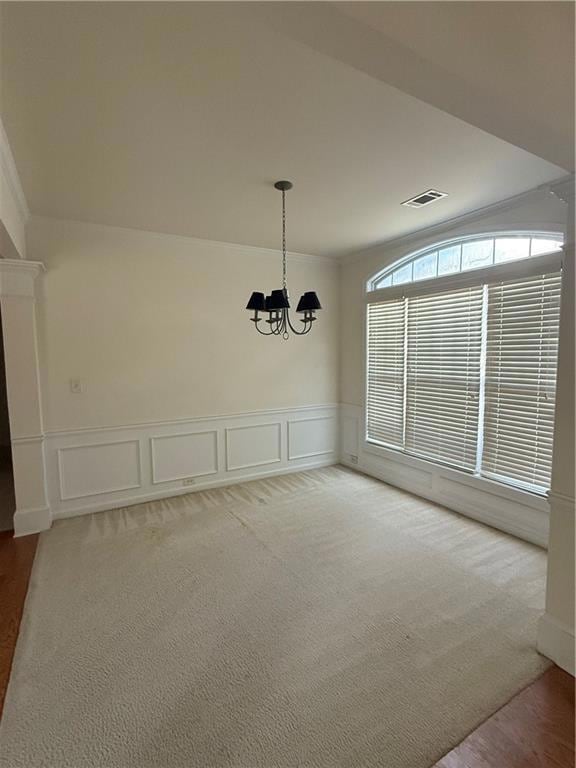 Unfurnished dining area with a chandelier, a decorative wall, ornamental molding, light carpet, and wainscoting