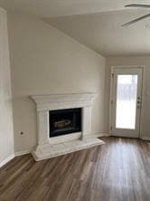 Unfurnished living room featuring a glass covered fireplace, dark wood-style flooring, and ceiling fan