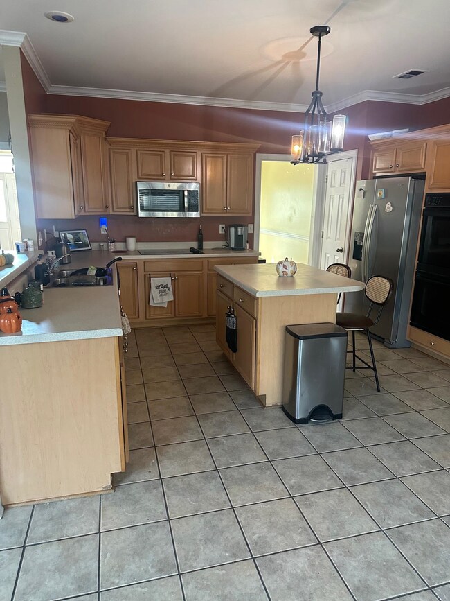 Kitchen featuring a breakfast bar area, light tile patterned floors, light countertops, ornamental molding, and black appliances