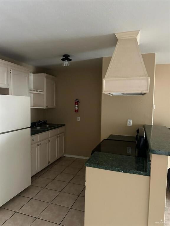 Kitchen with premium range hood, light tile patterned floors, white refrigerator, kitchen peninsula, and white cabinets