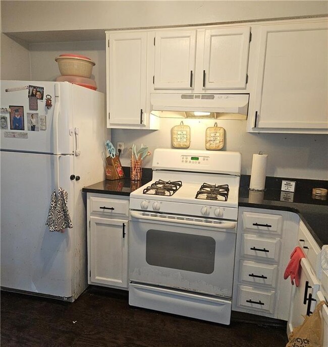 Kitchen with white appliances, under cabinet range hood, white cabinets, and dark countertops