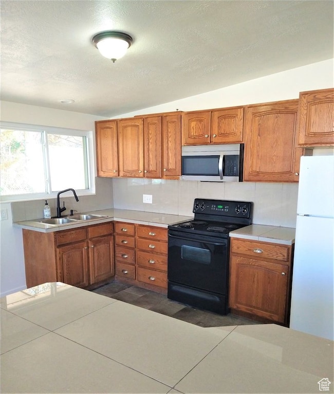 Kitchen featuring black electric range, freestanding refrigerator, light countertops, brown cabinets, and a textured ceiling