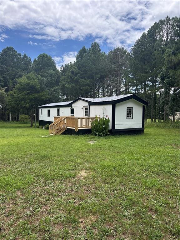 Front of house with a wooden deck, a lawn, and a view of trees