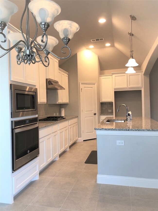 Kitchen featuring light stone counters, decorative light fixtures, decorative backsplash, appliances with stainless steel finishes, and white cabinetry