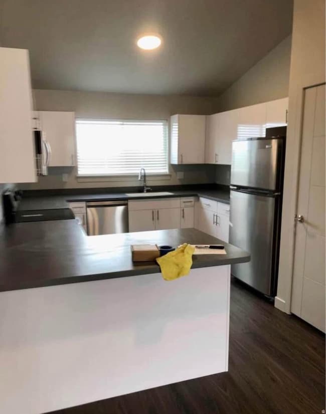 Kitchen featuring a peninsula, stainless steel appliances, dark countertops, dark wood finished floors, and white cabinetry