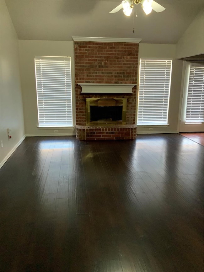 Unfurnished living room featuring lofted ceiling, a fireplace, ceiling fan, and dark wood-type flooring