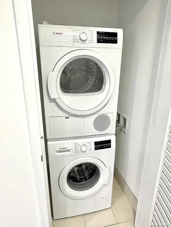 Laundry area featuring light tile patterned floors and stacked washing machine and dryer