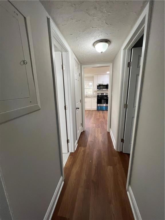 Hall with electric panel, dark wood-type flooring, a textured ceiling, and baseboards