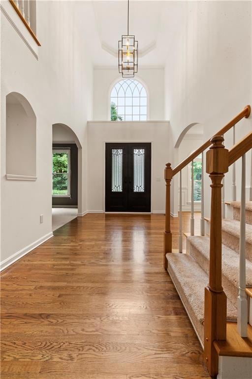 Foyer with a towering ceiling, arched walkways, french doors, wood finished floors, and stairs