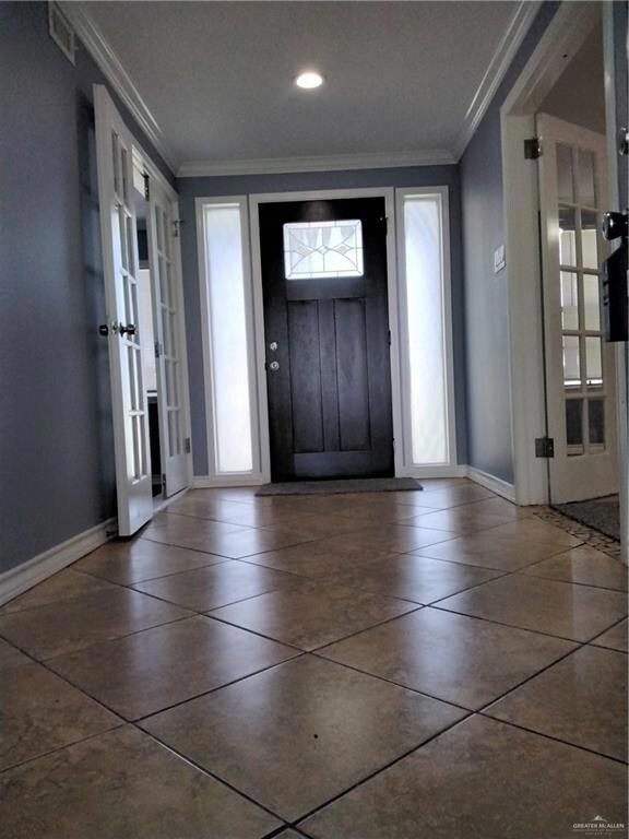 Foyer with crown molding, baseboards, and tile patterned floors