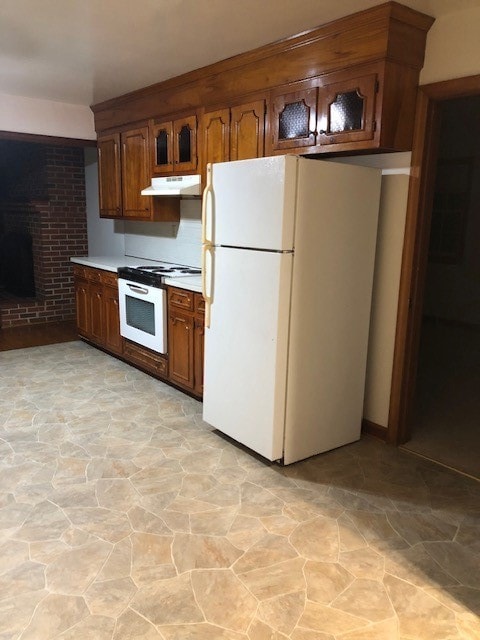 Kitchen with white appliances, light countertops, range hood, brown cabinetry, and light stone finish flooring
