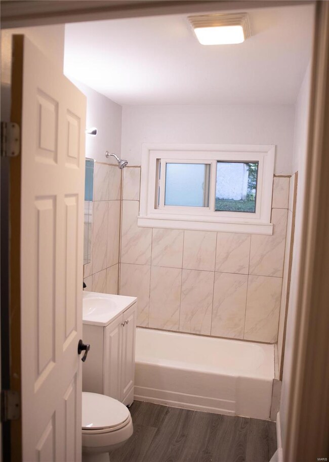 Full bathroom with hardwood / wood-style floors, tile walls, toilet, vanity, and tiled shower / bath combo