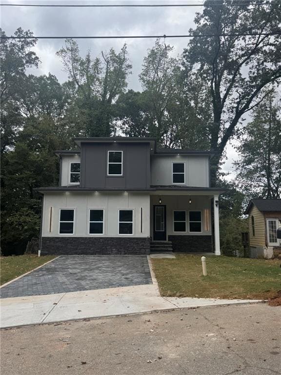 View of front of house featuring covered porch, stone siding, a front lawn, stucco siding, and driveway